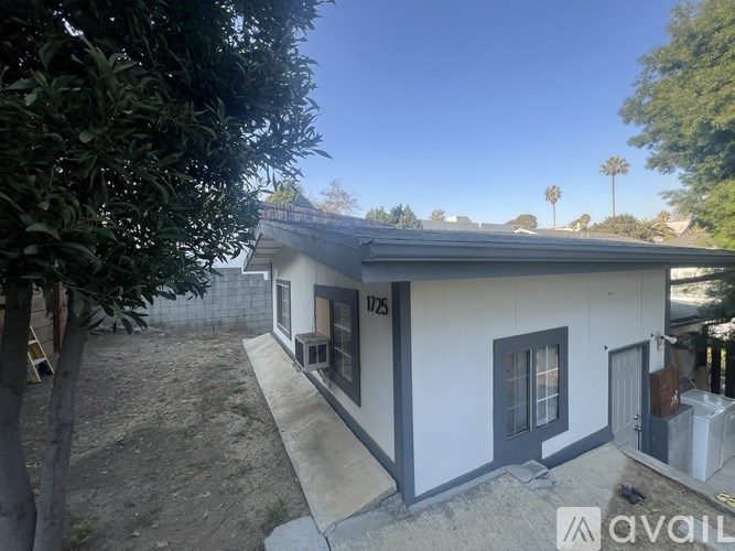 A house with a white exterior and a grey roof is surrounded by trees.
