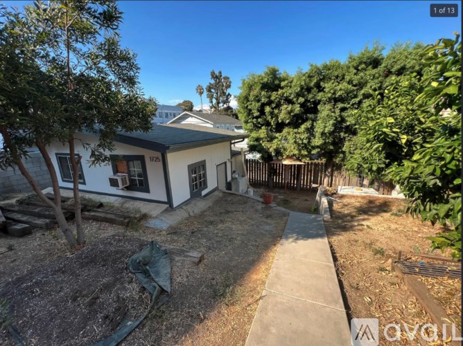 A white house with a brown roof and a tree in front of it.
