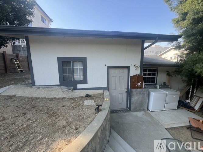 A white house with a black door and window is surrounded by a gravel area.
