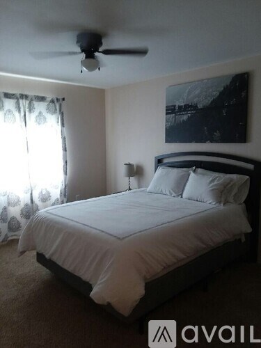 A bedroom with a bed, a ceiling fan, and a painting on the wall.