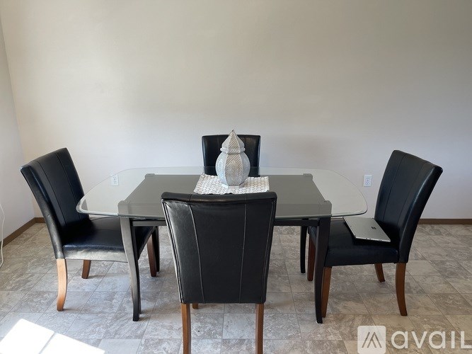 A glass dining table surrounded by black chairs.