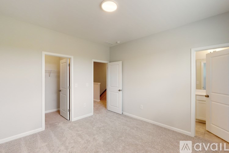 A room with white walls and carpeted floor with a door open to another room.