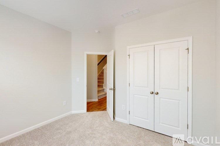 A white room with a carpeted floor, a white door, and a staircase.
