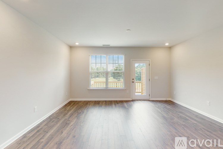 A spacious room with wooden floors and a large window overlooking a balcony.