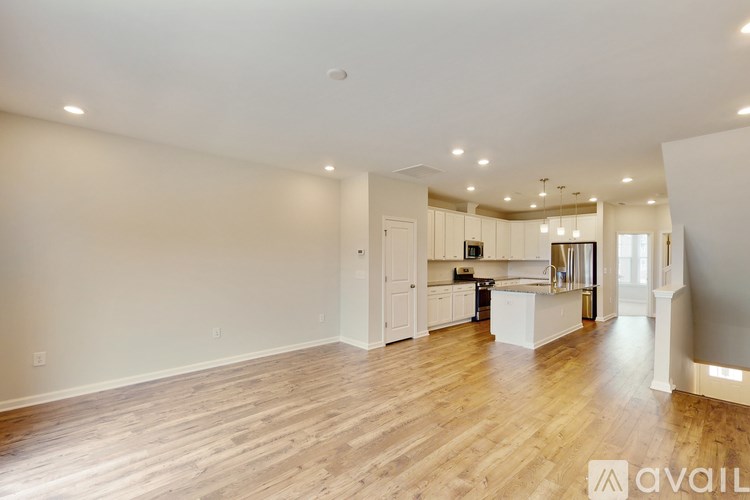 A spacious living room with wooden flooring and a kitchen in the background.