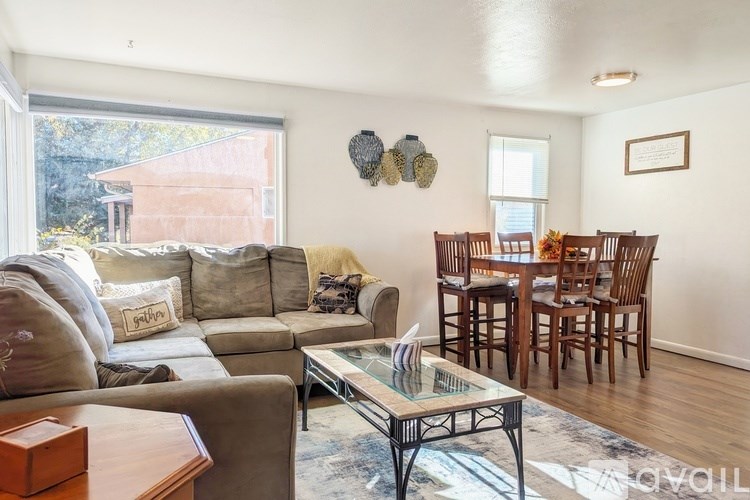 A living room with a grey couch, a glass coffee table, and a dining table with chairs.