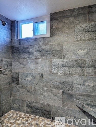 A bathroom with a grey tiled wall and a window.