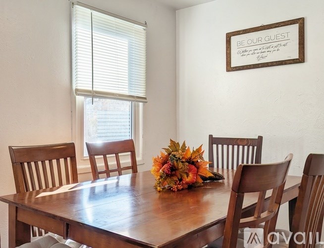 A wooden dining table with chairs and a sign that says "Be Our Guest" on the wall.