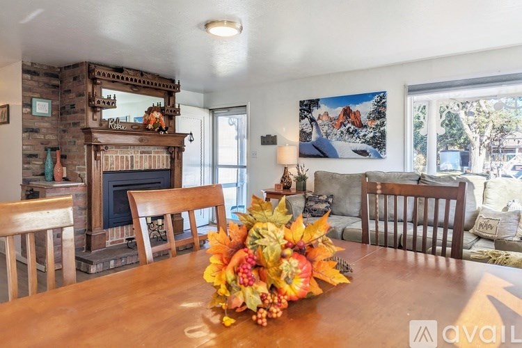 A wooden table with a fall floral centerpiece in the middle of a room with a fireplace and chairs.