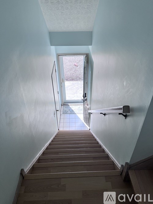 A stairway with a light blue wall and wooden steps leading to a door.