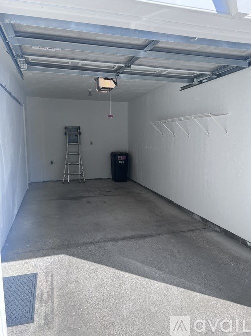 A large empty garage with a ladder and a trash can.