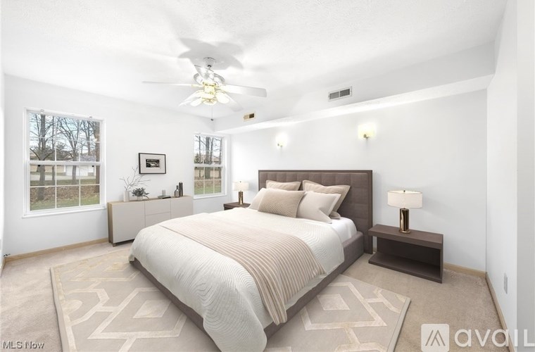 A bedroom with a large bed, a ceiling fan, and a window with a view of trees.