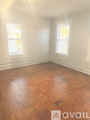 A room with wooden flooring and two windows.