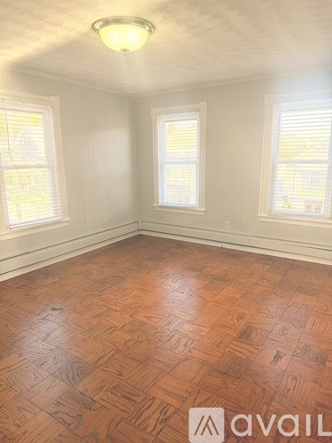A room with wooden flooring and two windows.