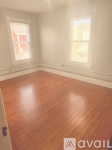 A room with wooden flooring and two windows.