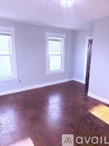 A room with wooden flooring and two windows.