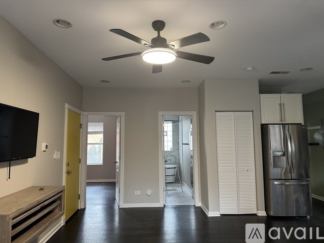 A spacious room with a ceiling fan and a refrigerator on the right side.