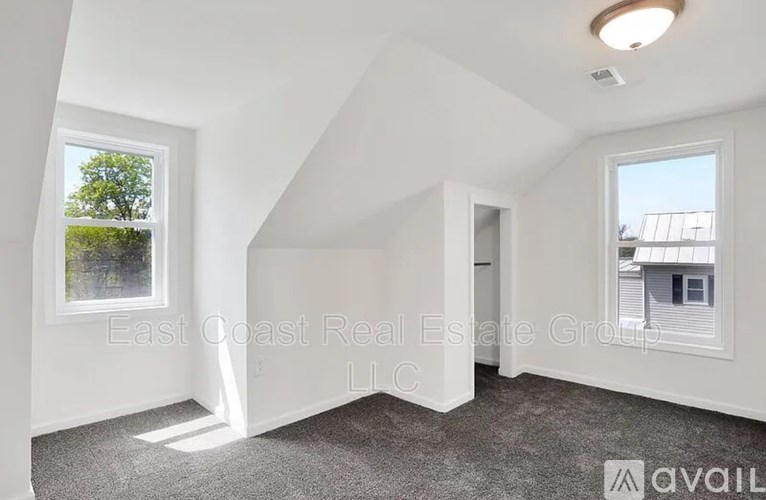 A room with white walls and a window showing a tree and a house.