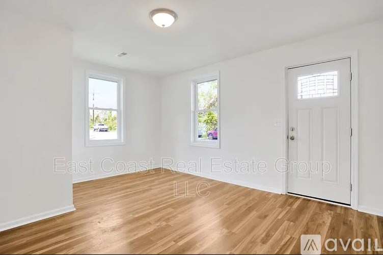 A room with wooden flooring and white walls, with a door on the right and a window on the left.