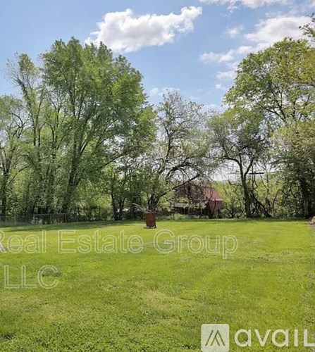 A grassy field with trees and a house in the background.