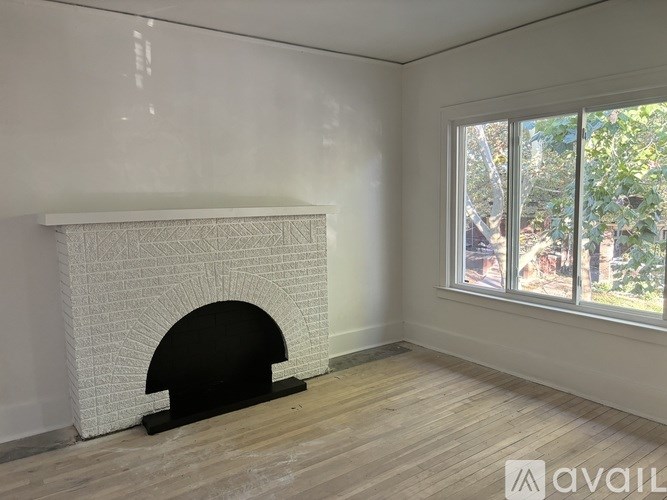 A white fireplace in a room with wooden flooring and a window.