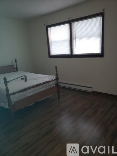 A bedroom with a bed, wooden floors, and a window with blinds.