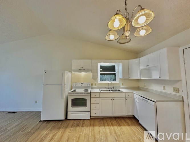 A kitchen with white appliances and cabinets, a window, and a wooden floor.