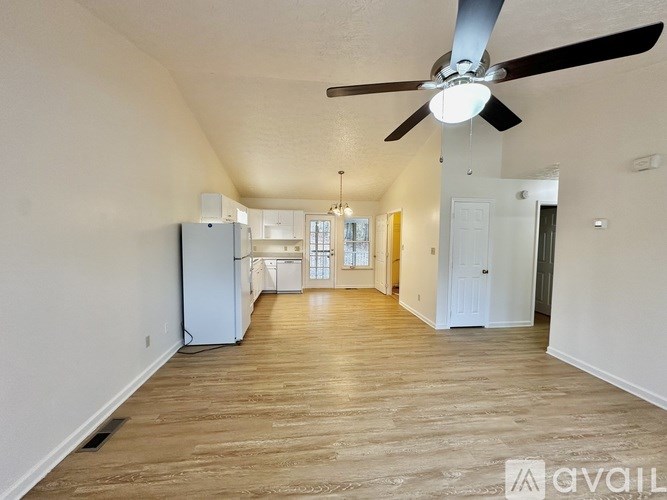 A spacious room with a ceiling fan and light, hardwood floors, and a white refrigerator.