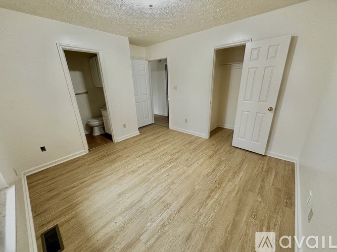 A room with wooden flooring and white walls, with a door and a window.
