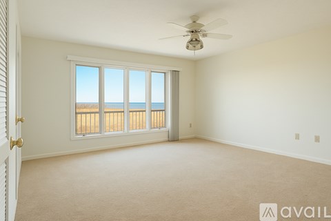 A room with a carpeted floor, a ceiling fan, and a window overlooking the beach.