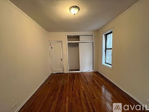 A room with wooden floors and white walls, with a window on the right side.