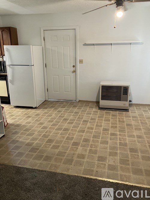 A room with a white refrigerator, a door, a fan, and a wall-mounted shelf.