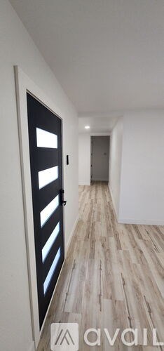 A hallway with a black door and wooden flooring.