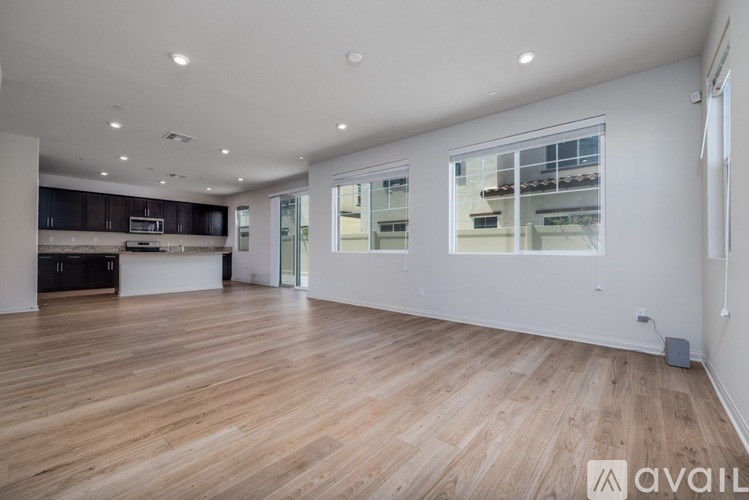 A spacious room with wooden flooring and a kitchen area in the background.