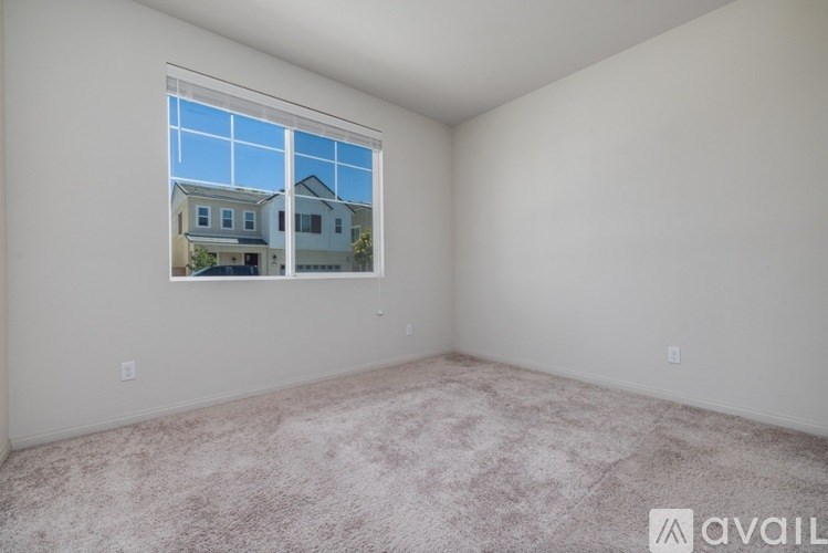 A room with a carpeted floor and a window showing a view of a house across the street.