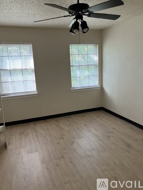 A room with a ceiling fan and two windows.