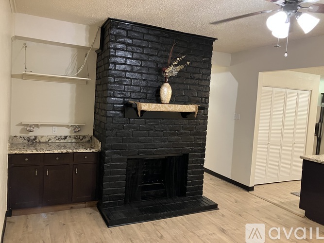 A black brick fireplace with a shelf above it and a fan on the ceiling.