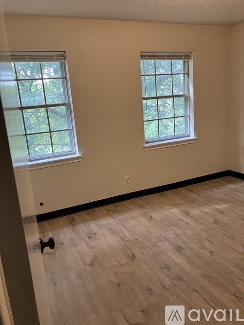A room with wooden flooring and two windows.