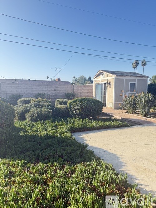 A house with a grey roof and a white door is surrounded by green bushes.