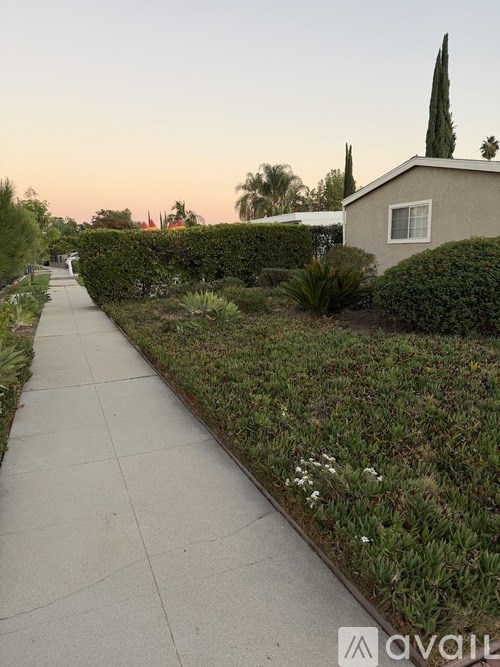 A sidewalk runs alongside a well-manicured hedge in front of a house.