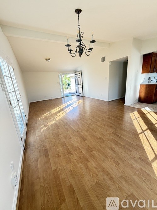 A large empty room with wooden flooring and a chandelier.