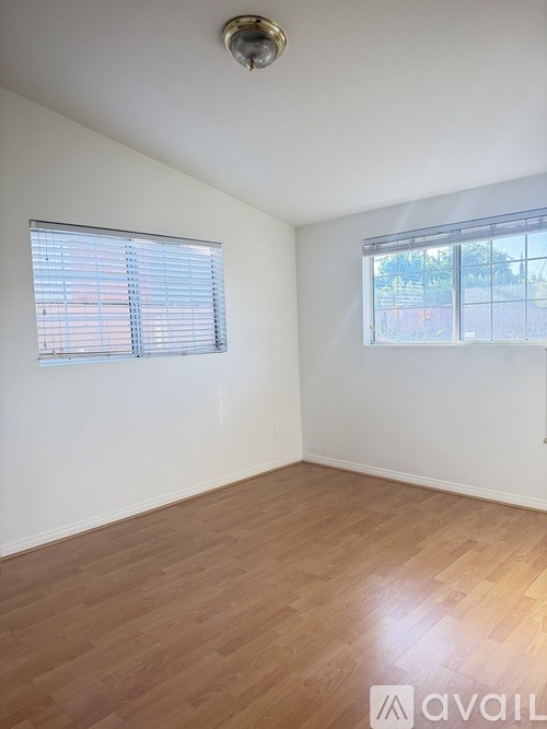 A room with wooden flooring and two windows.