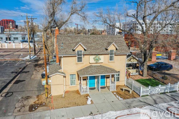 A house with a brown roof and a blue door is surrounded by a white picket fence.