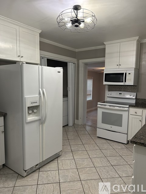 A white refrigerator is in a kitchen with white cabinets.