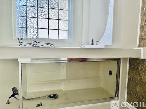 A white bathroom with a glass shower door and a window.