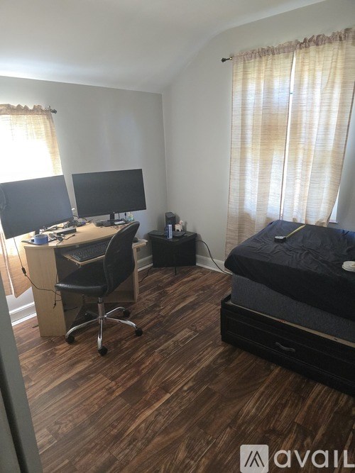 A bedroom with a bed, desk, and two monitors.