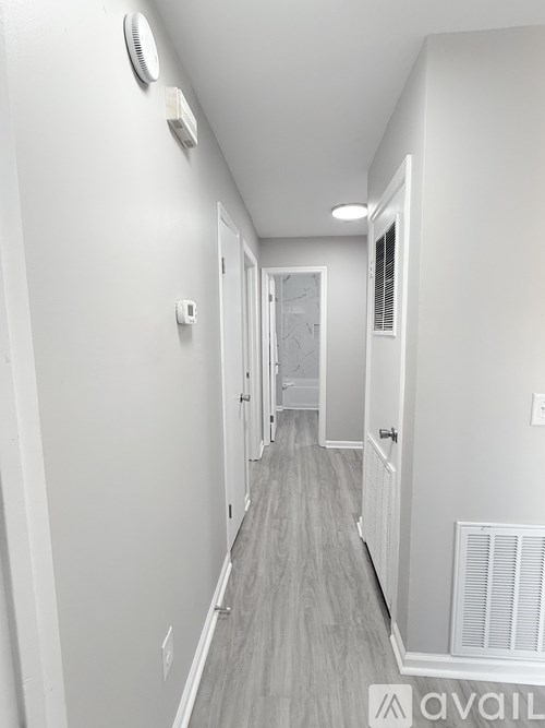 A long hallway with a light on the wall and a door at the end.