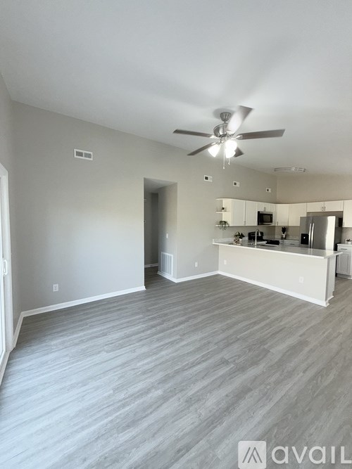 A spacious room with a ceiling fan and a kitchen area in the background.