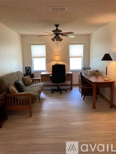 A living room with a couch, chair, desk, and a fan.