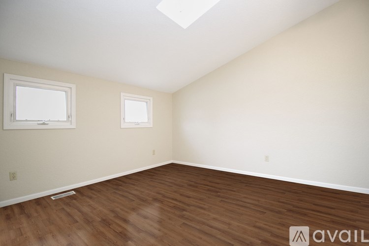 A room with wooden flooring and two windows.